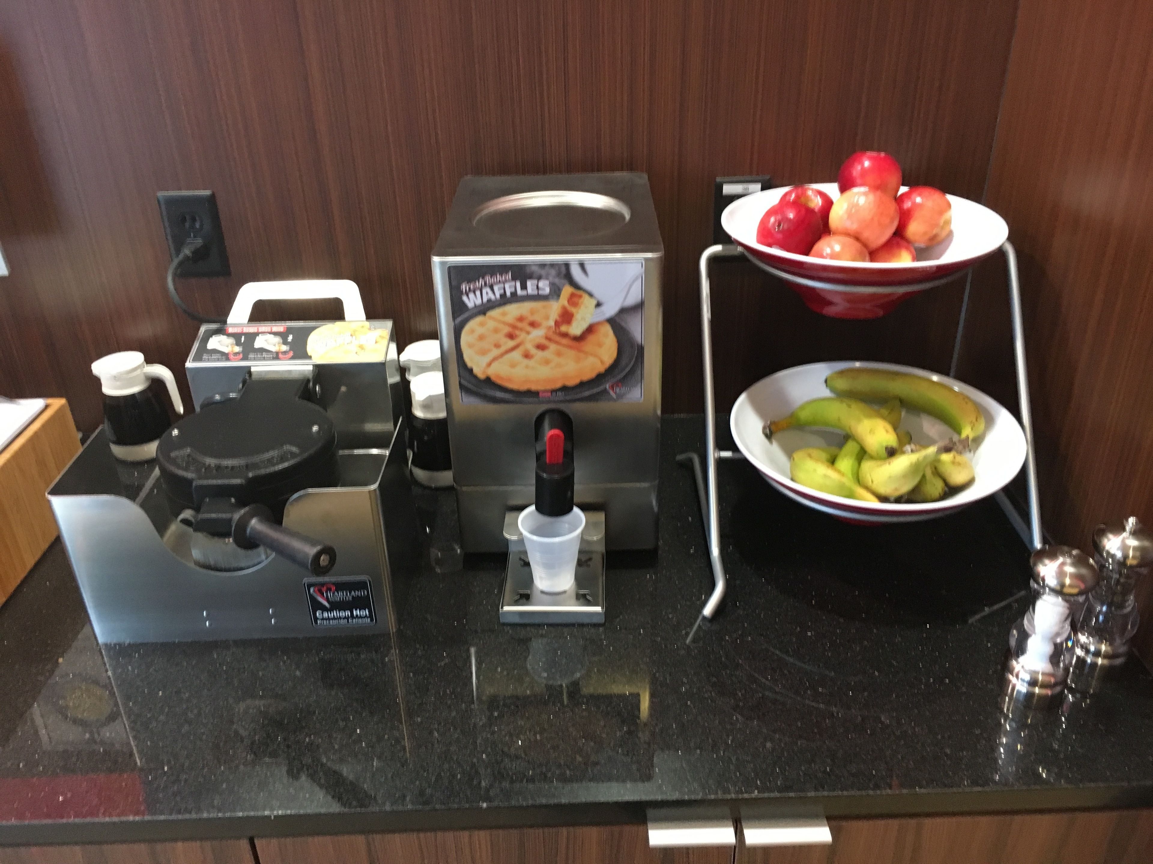 Eine Küchenarbeitsfläche mit einem Waffeleisen, einer Kaffeemaschine und einer Schüssel Obst.