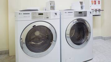 Deux lave-linge professionnels de marque LG dans une buanderie, avec un sol carrelé et un panneau affiché sur le mur.
