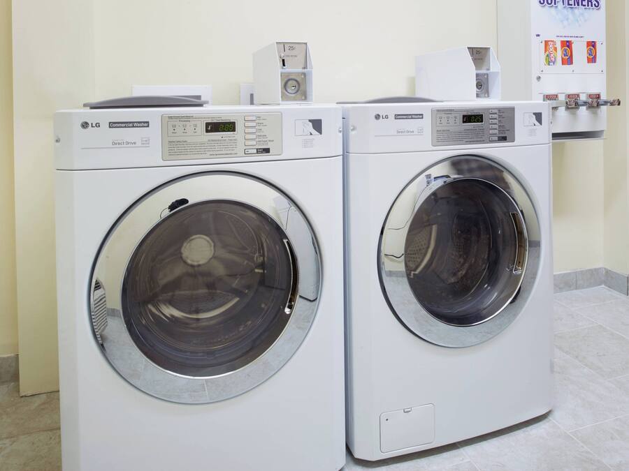 Deux lave-linge professionnels de marque LG dans une buanderie, avec un sol carrelé et un panneau affiché sur le mur.