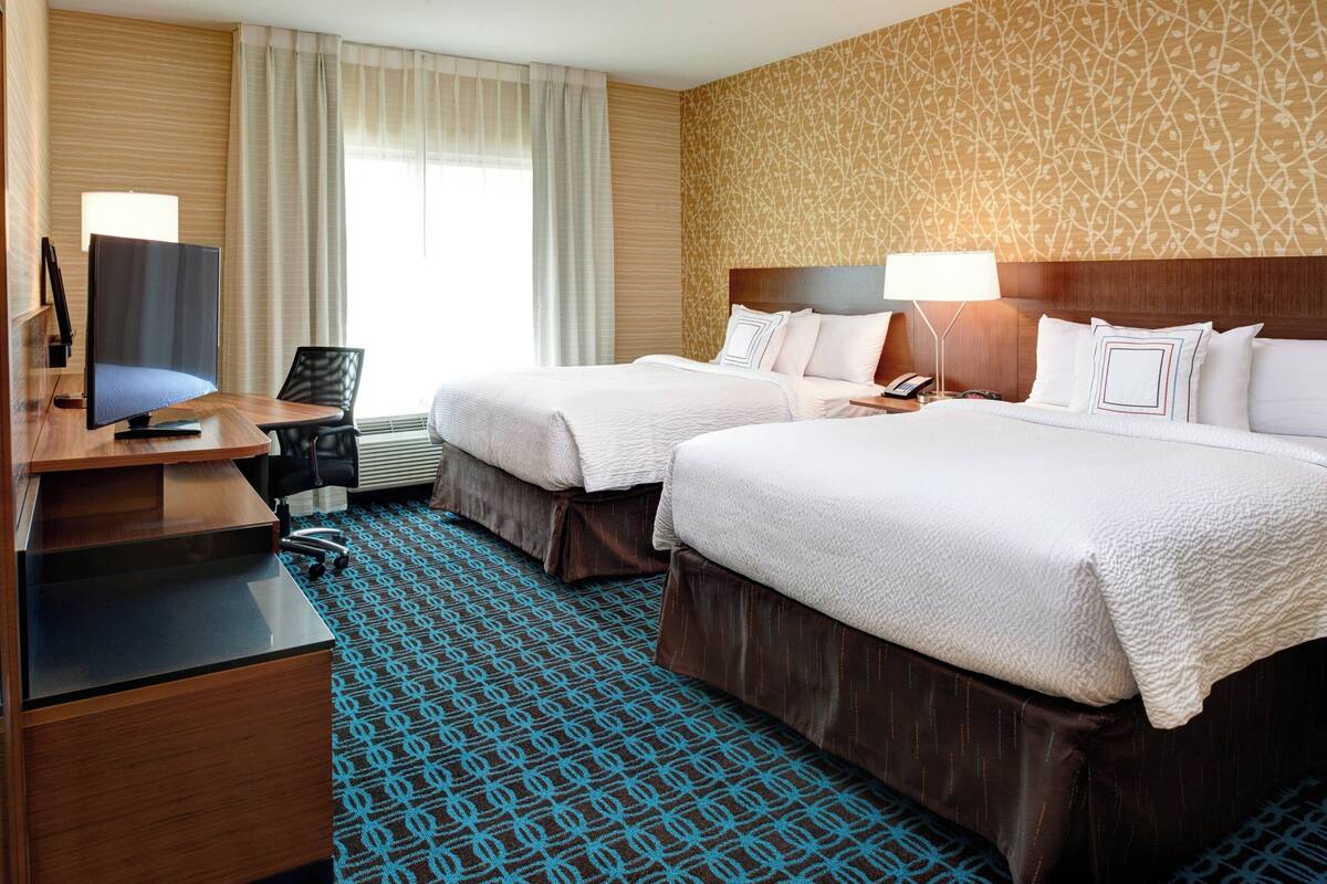 A hotel room with two beds, a desk, a TV, and a patterned carpet.