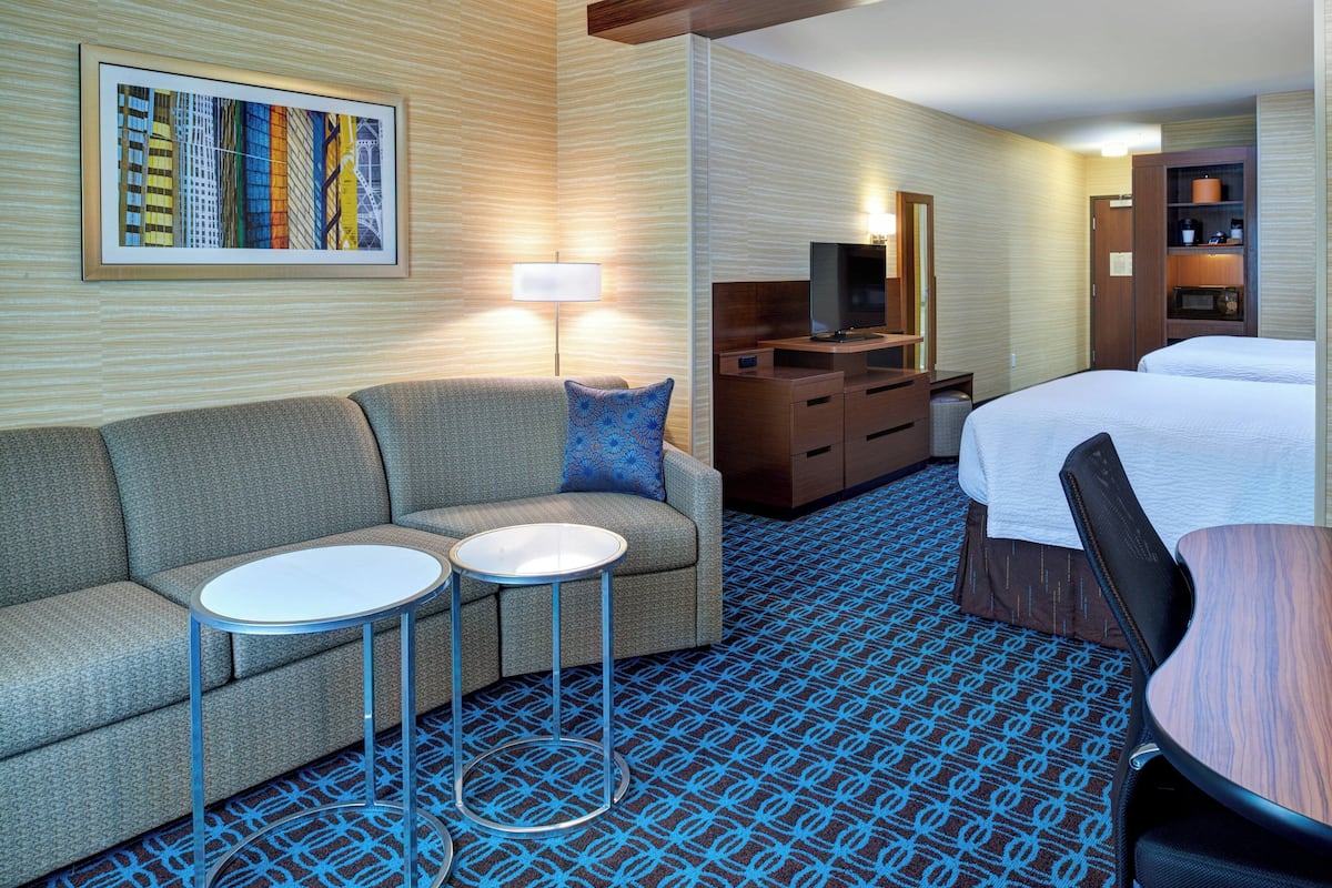 A hotel room with a sofa, two small tables, a bed, a TV, a mirror, and a wardrobe.