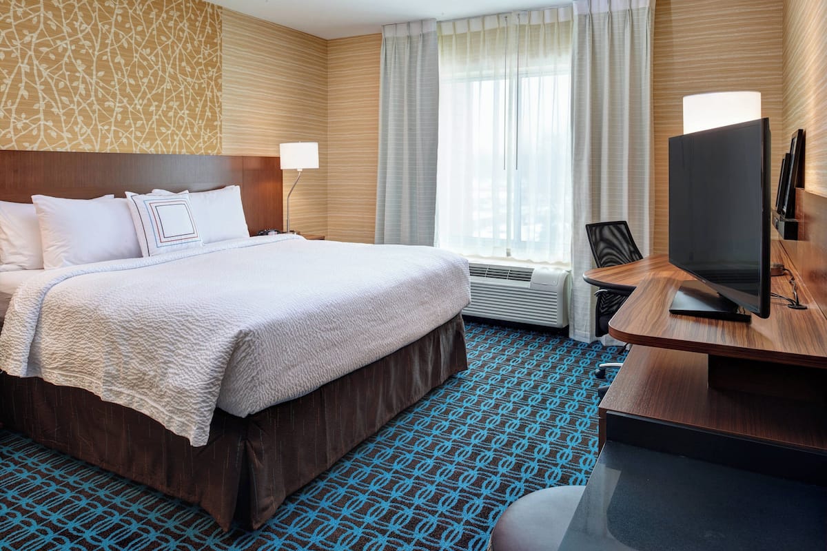 A hotel room with a large bed, a desk with a flat-screen TV, a chair, and a window with curtains.