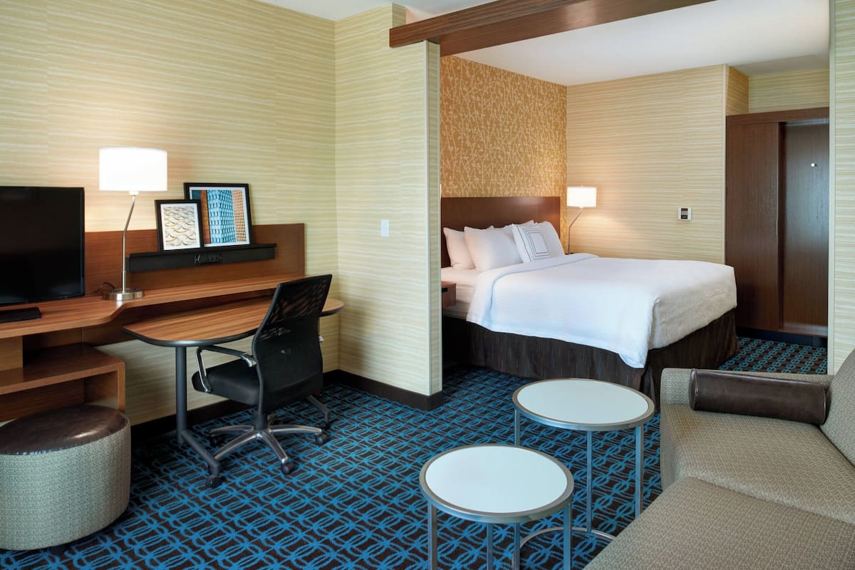 A hotel room with a bed, a desk, a chair, a television, and two small tables.