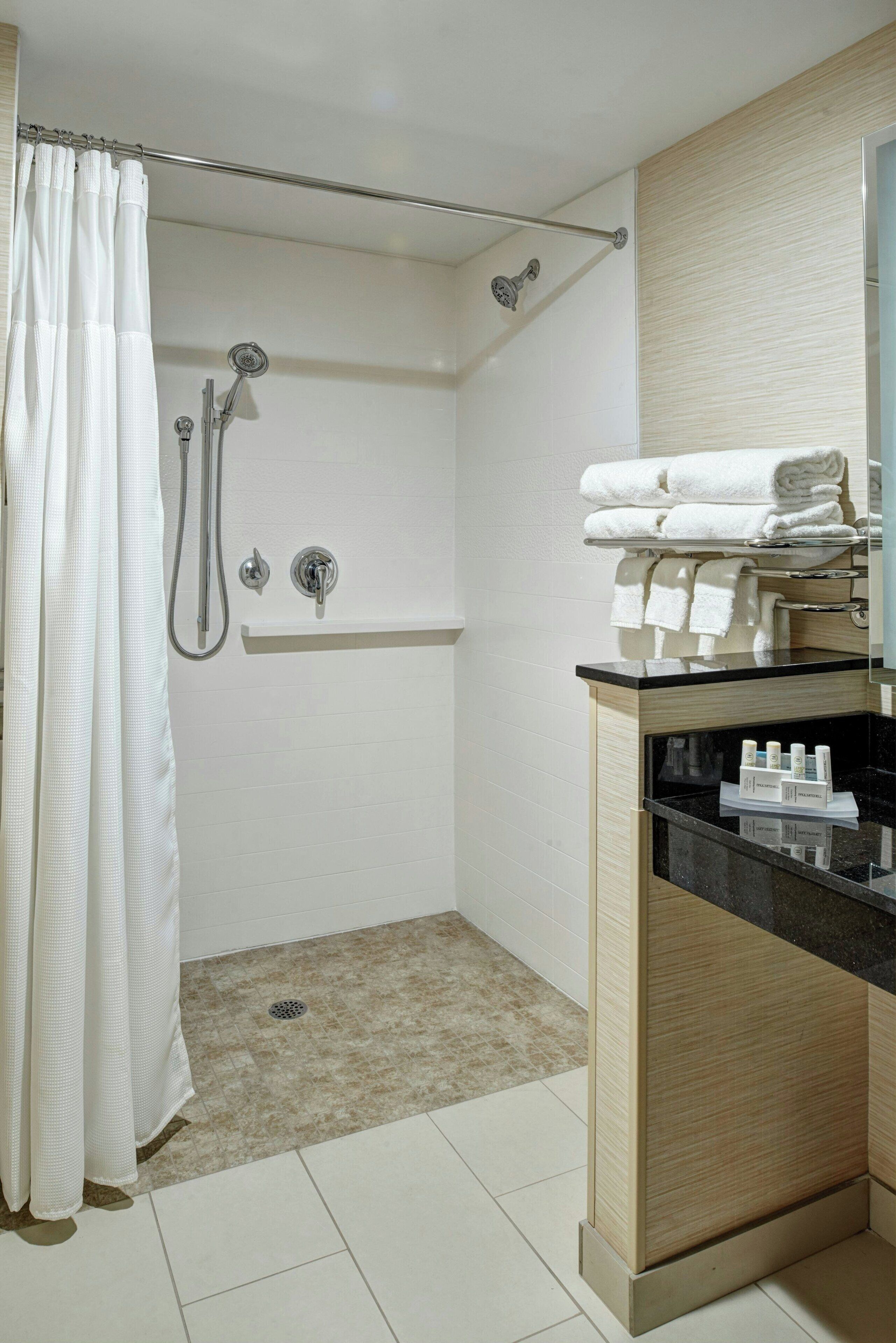 Un baño moderno con ducha, tocador con mampara de vidrio y toallas ordenadas en un estante.