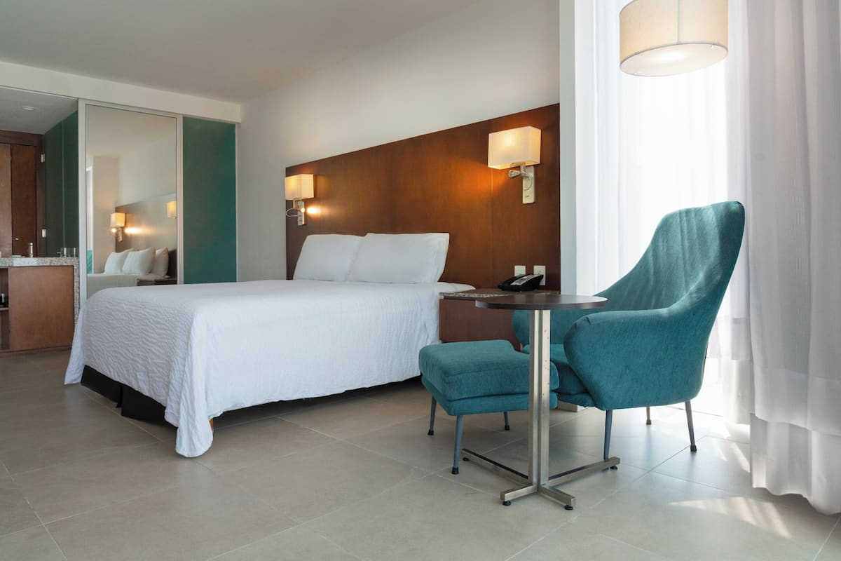 Una habitación de hotel con cama, escritorio, silla y espejo.