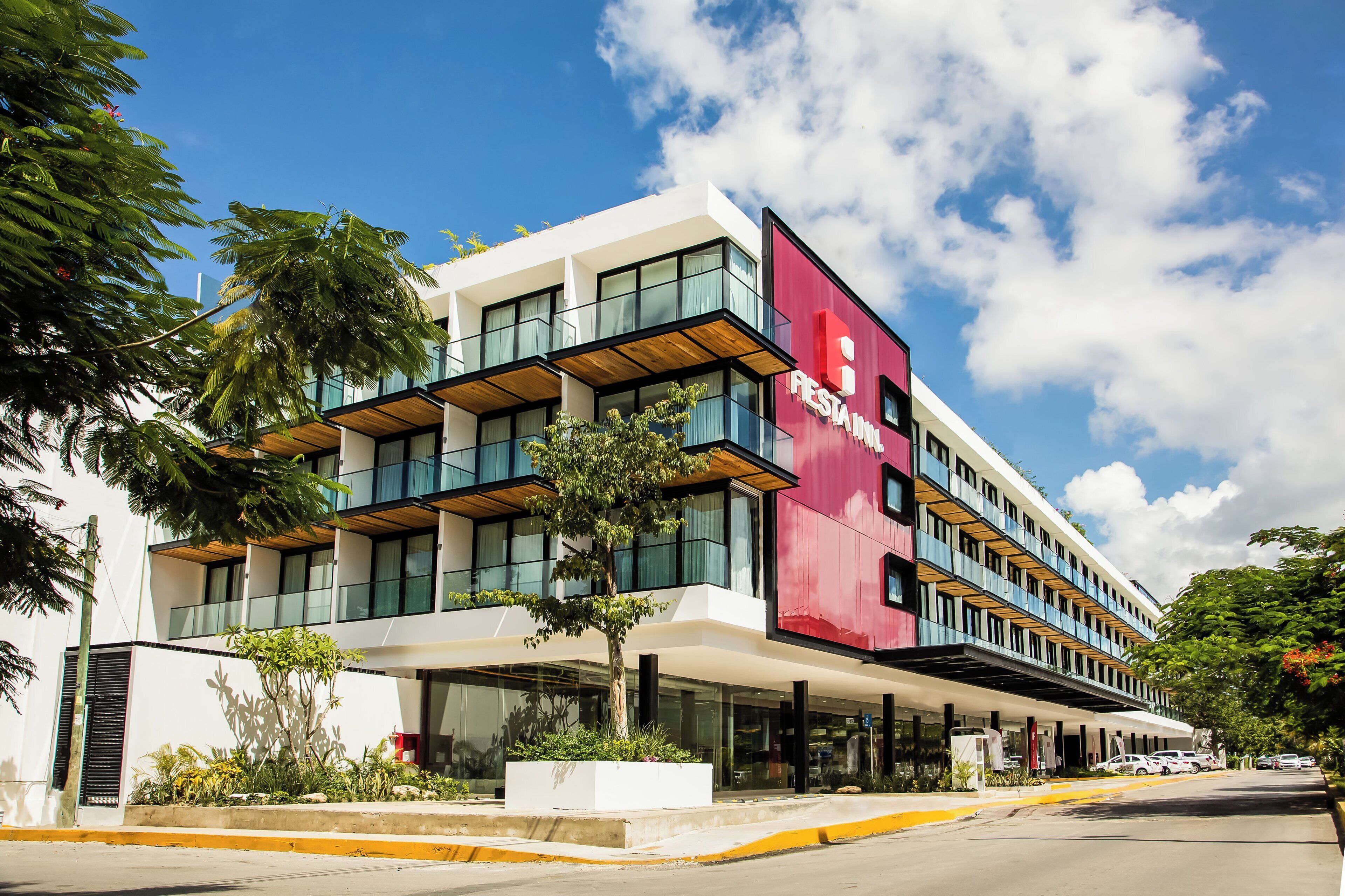 Un hôtel moderne à la façade rouge et blanche, doté de nombreux balcons et d’un espace d’entrée abrité.