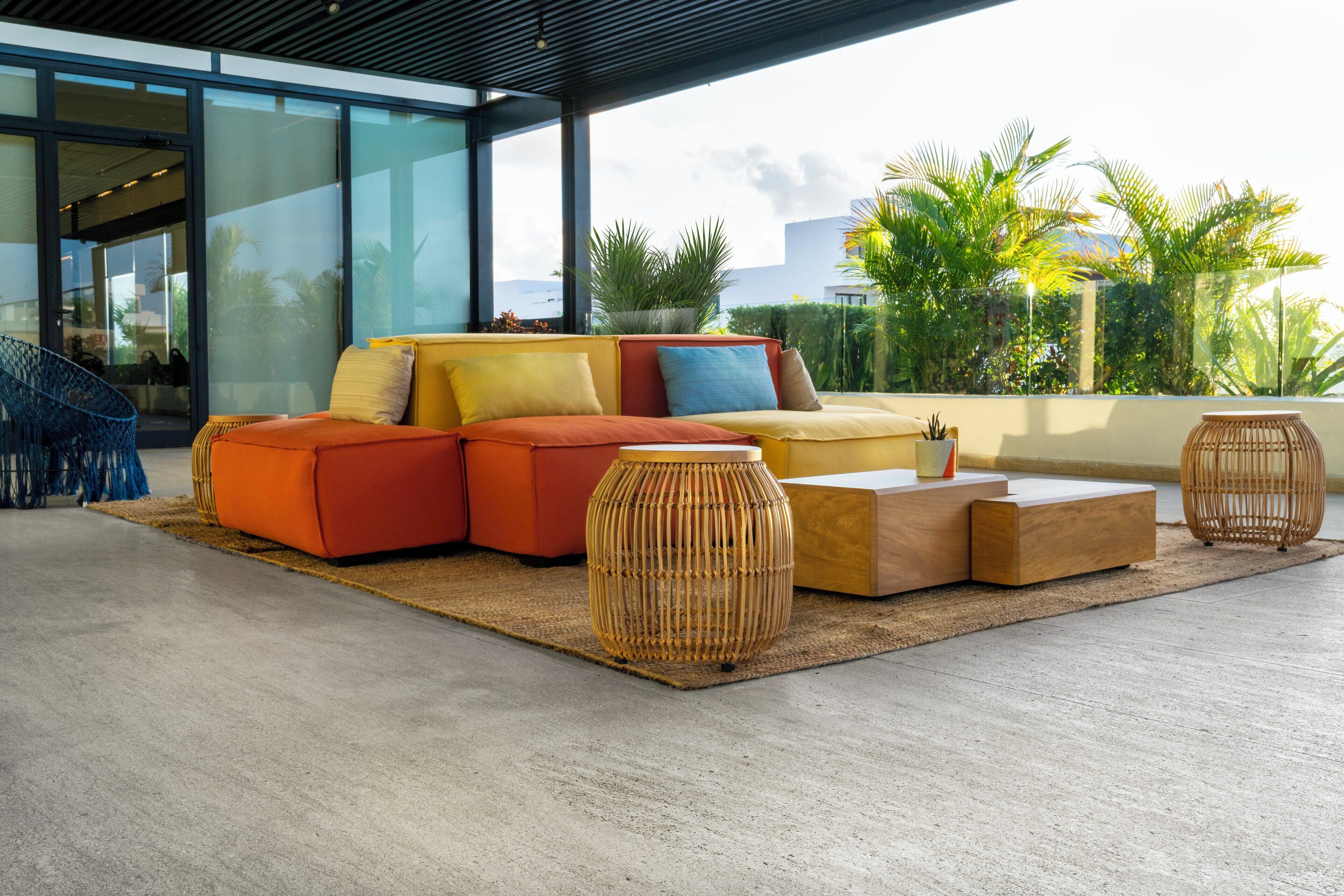Un espace de détente extérieur moderne, comprenant un canapé d’angle, deux petites tables d’appoint et une vue sur des palmiers et des immeubles.