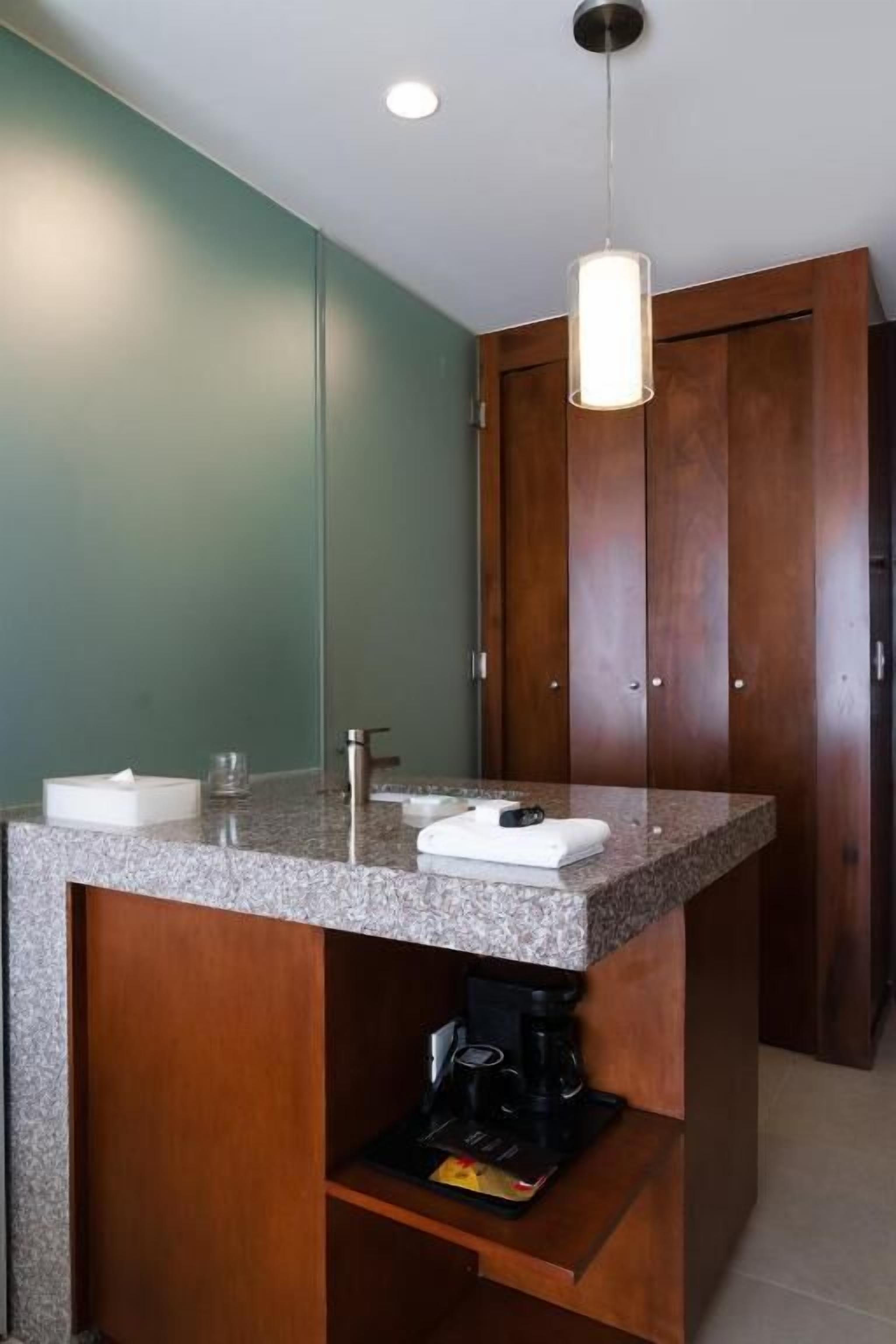 Bagno con lavabo in ceramica bianca, specchio e porta in legno, e piano di lavoro in granito.