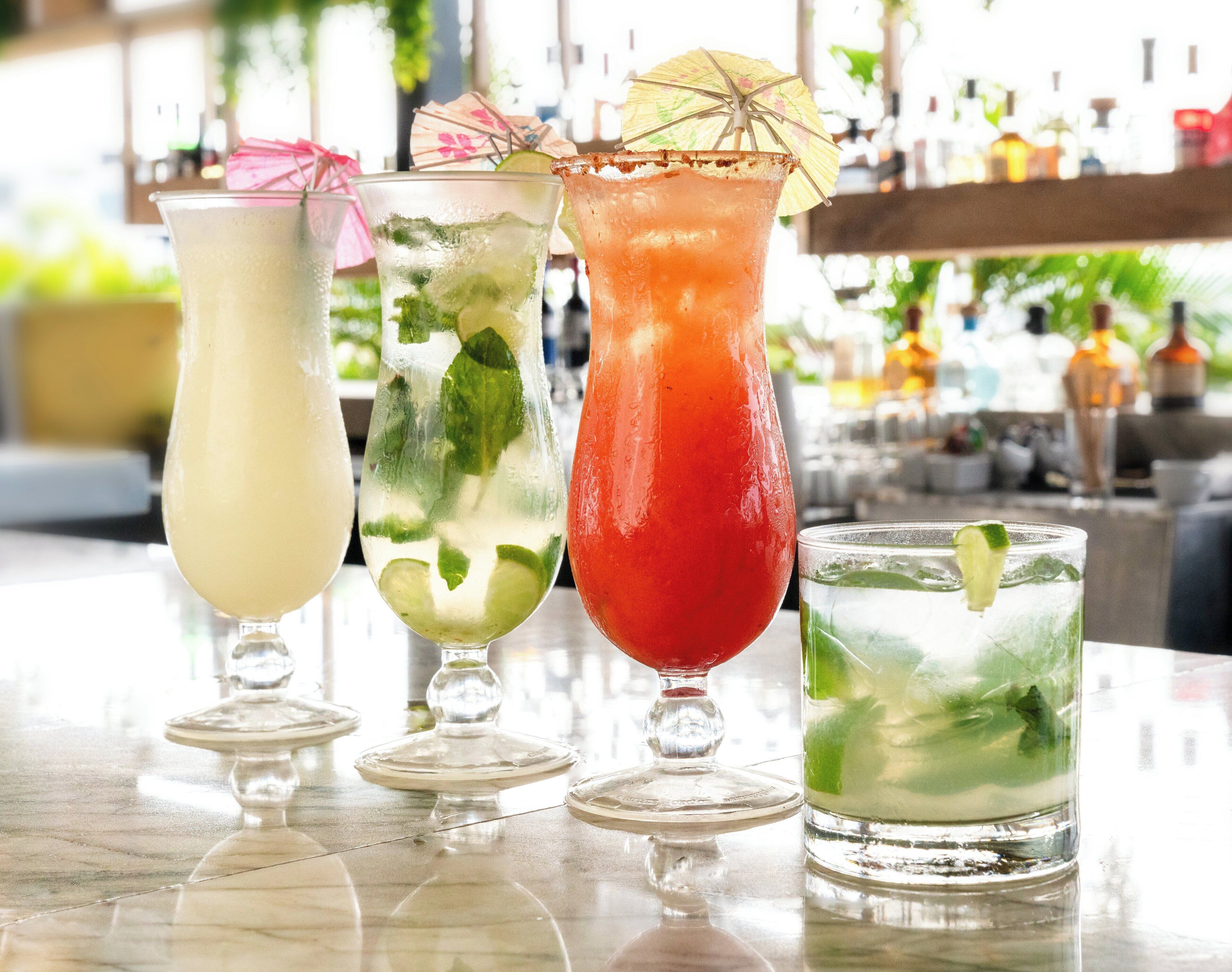 Four different cocktails on a bar counter with a blurred background of a bar area.