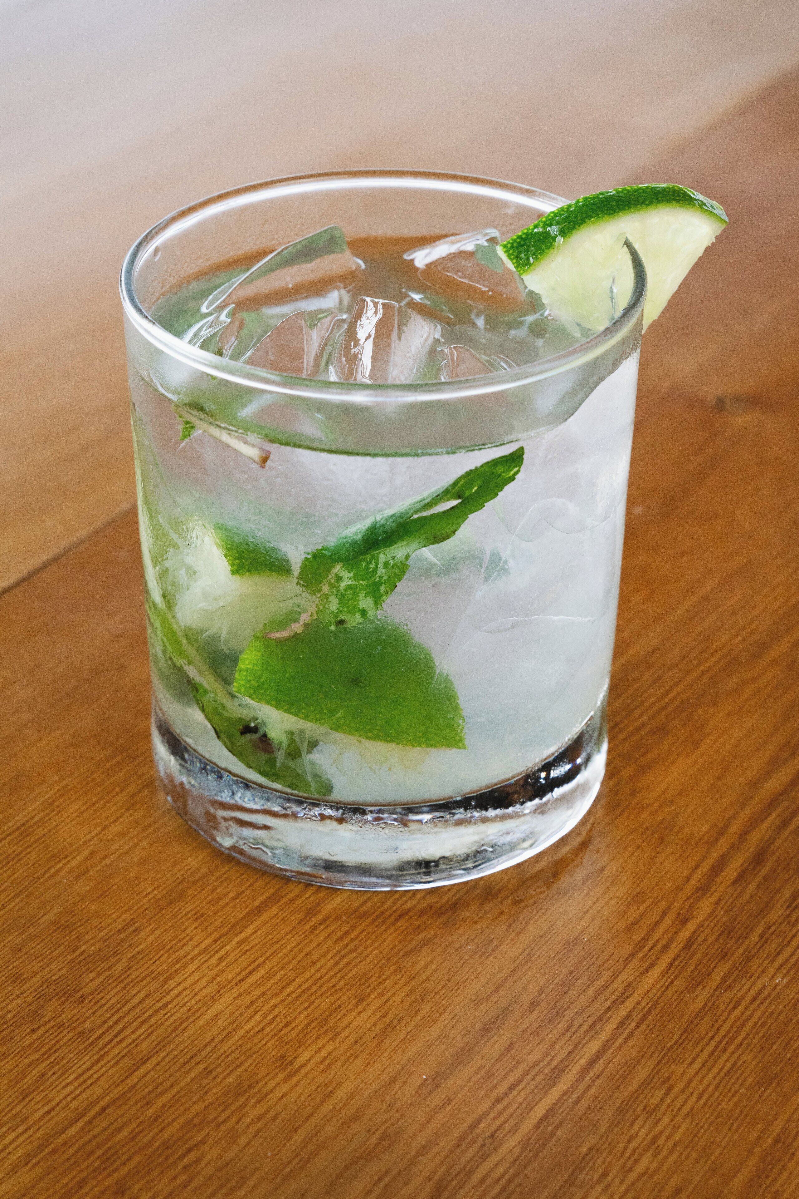 A glass of iced drink with lime and mint on a wooden table.