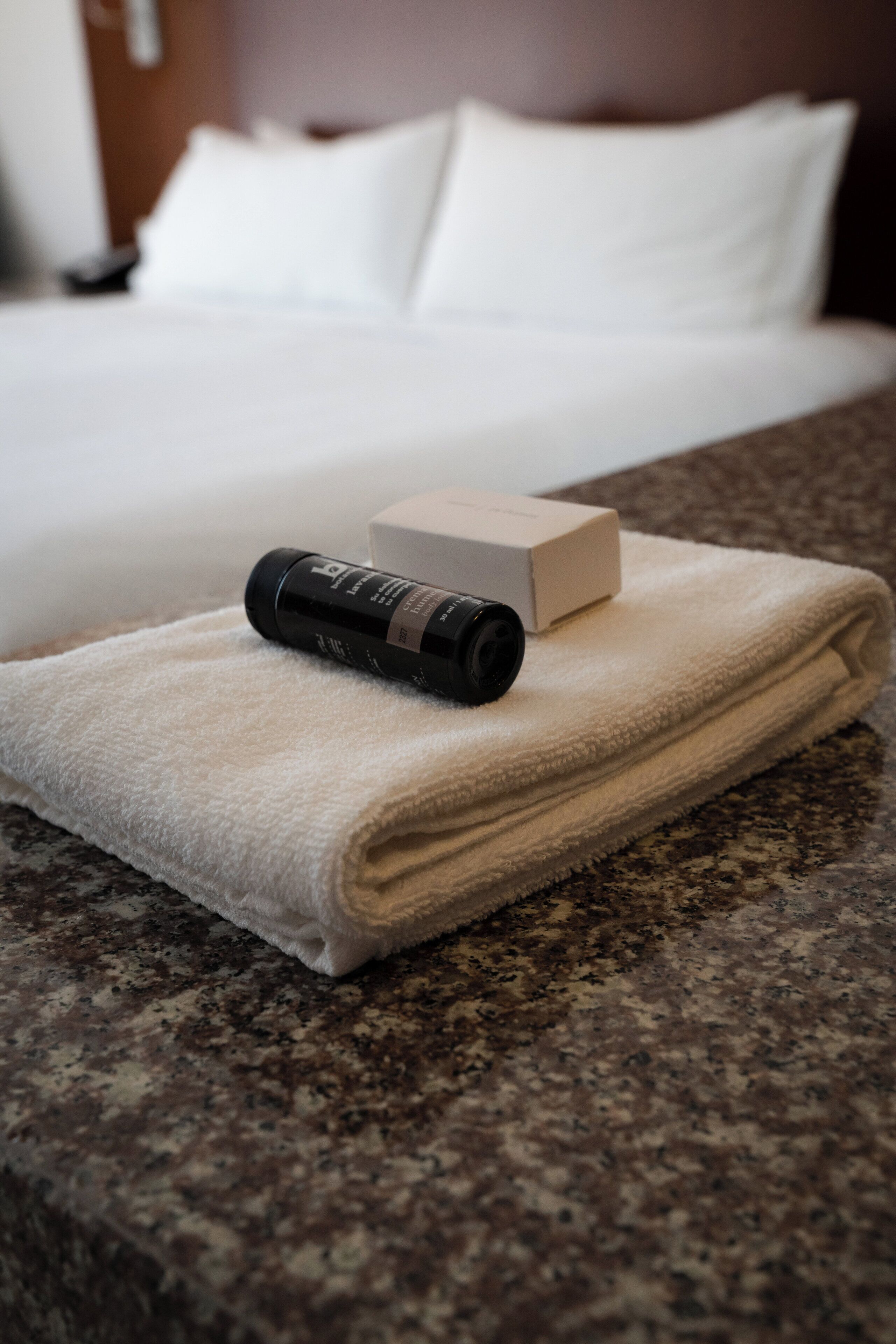 A neatly folded white towel on a granite countertop with a black cylindrical object and a beige box on top.