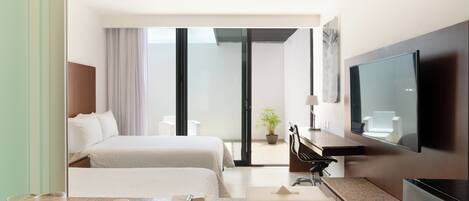 A hotel room with two beds, a flat-screen TV, a desk with a chair, a potted plant, and a sliding glass door leading to a balcony.