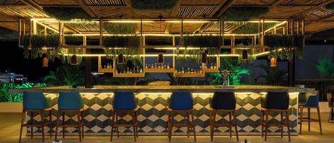 A bar area with a geometric patterned wall, wooden ceiling, and hanging plants.