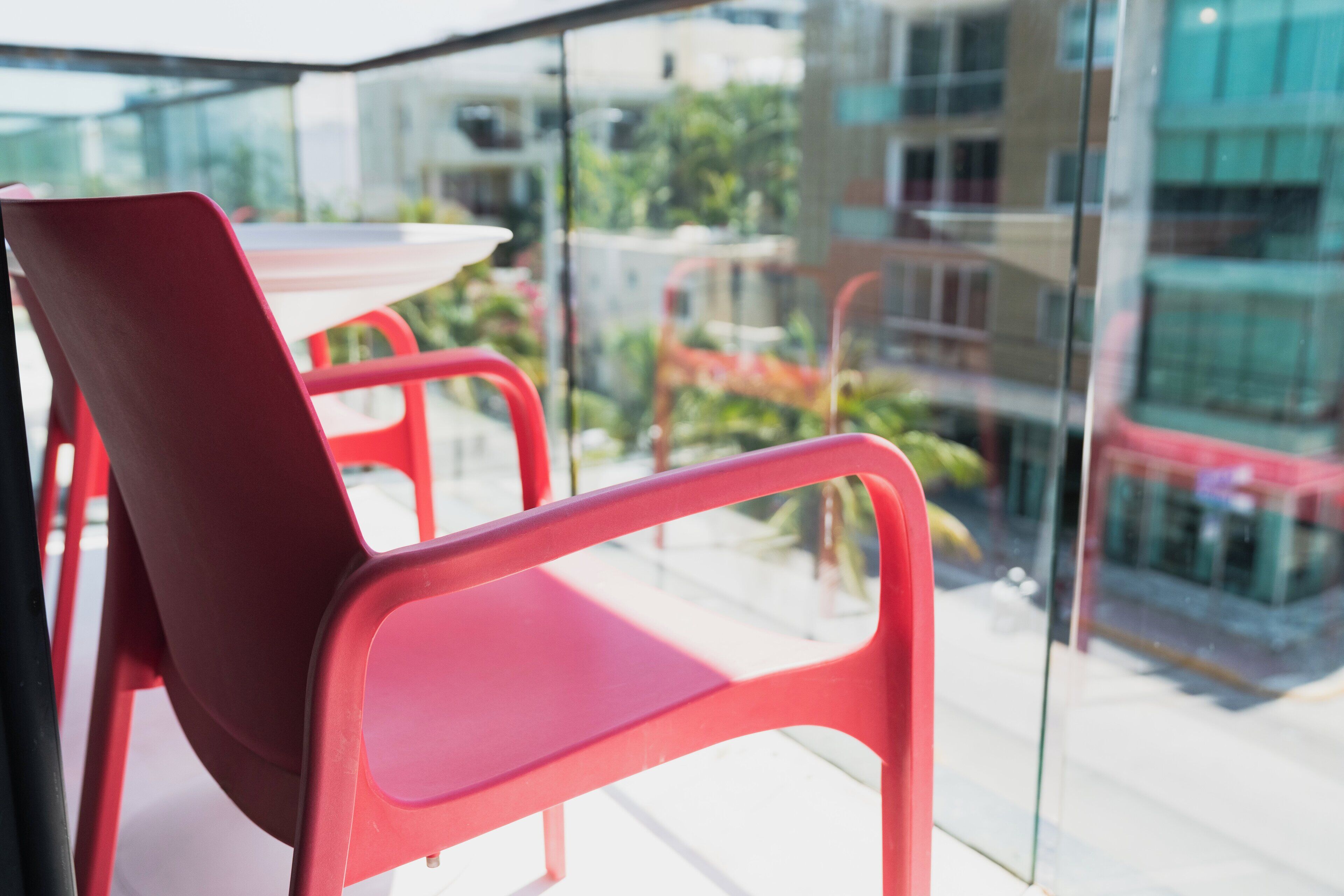 A red chair and table on a balcony with a view of buildings and greenery.