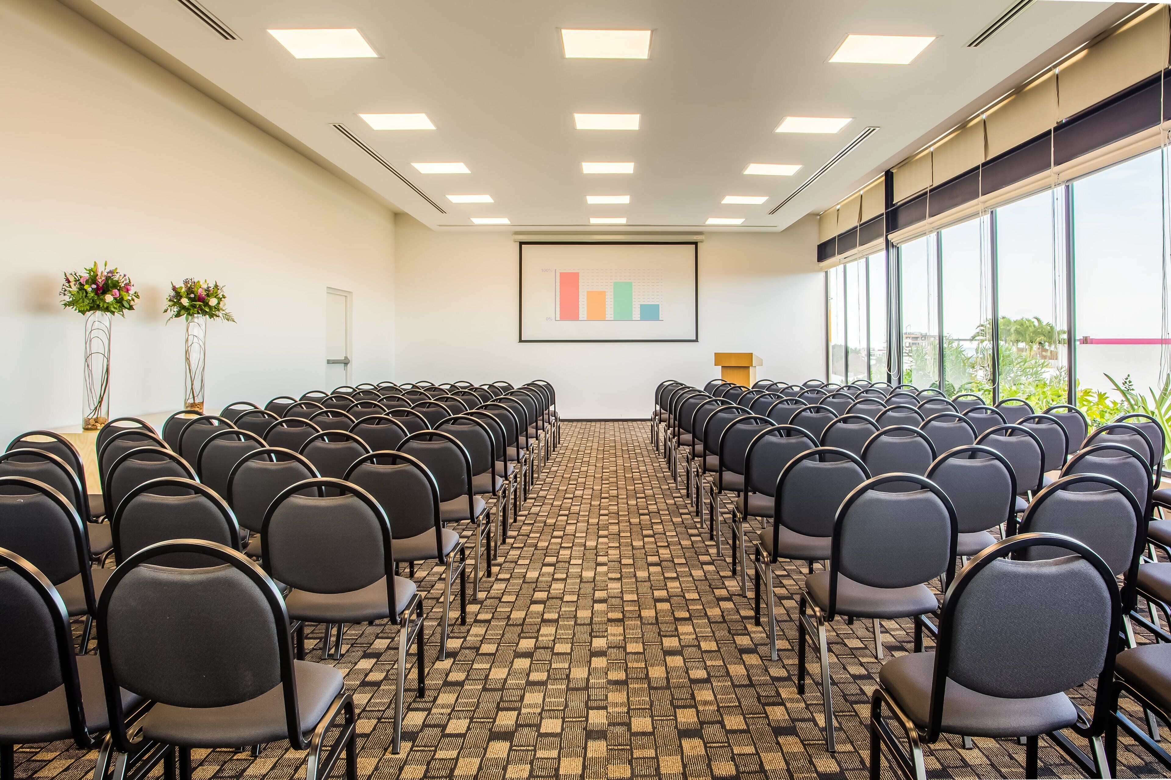 Ein Konferenzraum mit Reihen von Stühlen, einer Projektionsleinwand und einem großen Fenster mit Blick.