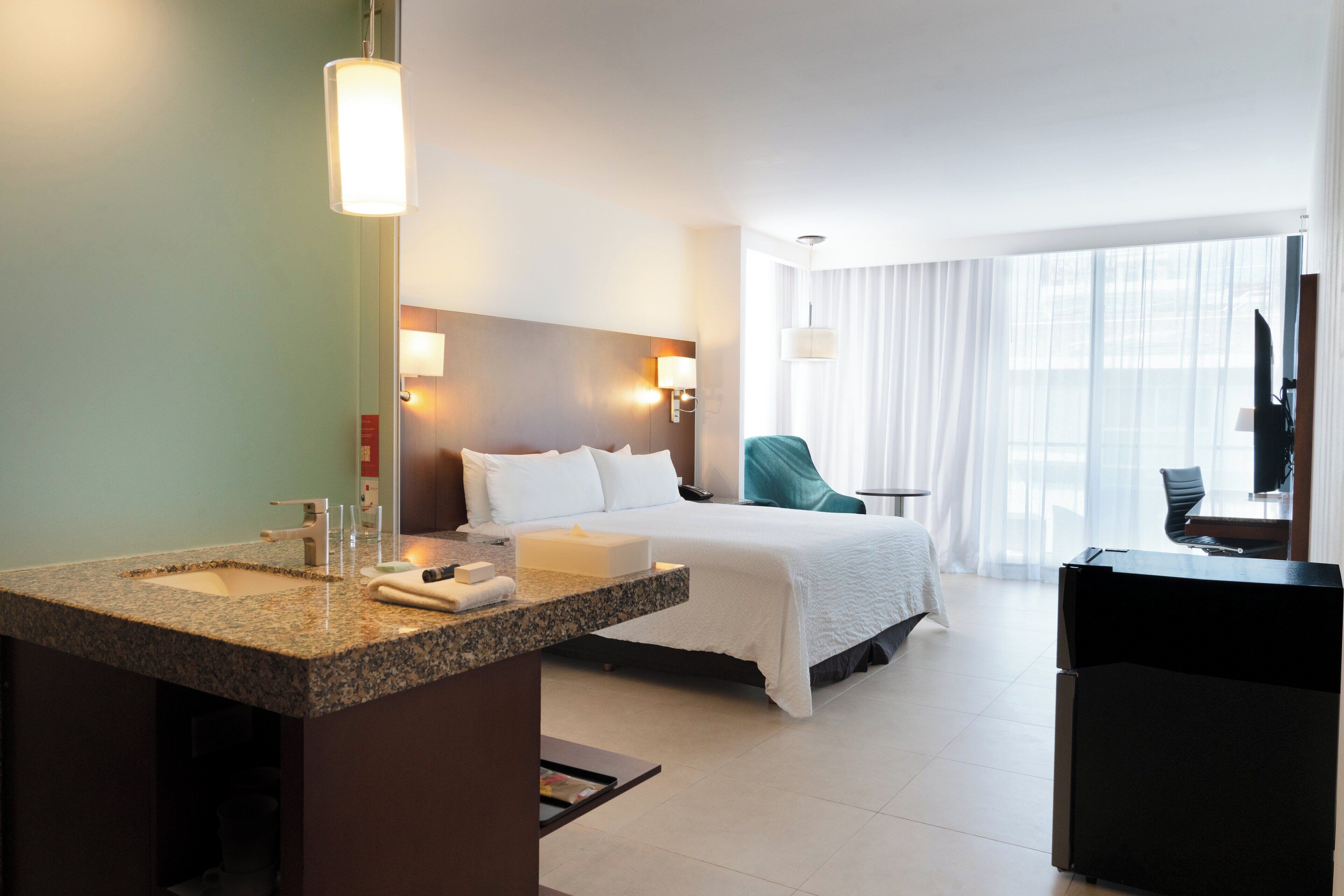 Une chambre d’hôtel comprenant un lit, un bureau, une chaise, une télévision et une salle de bain avec un lavabo et un miroir.