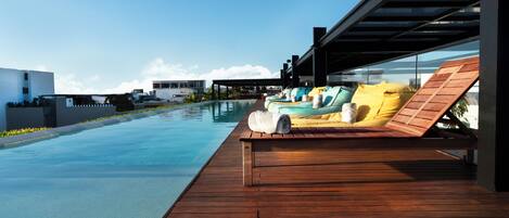 Terraza de madera con sillones de descanso y una piscina.