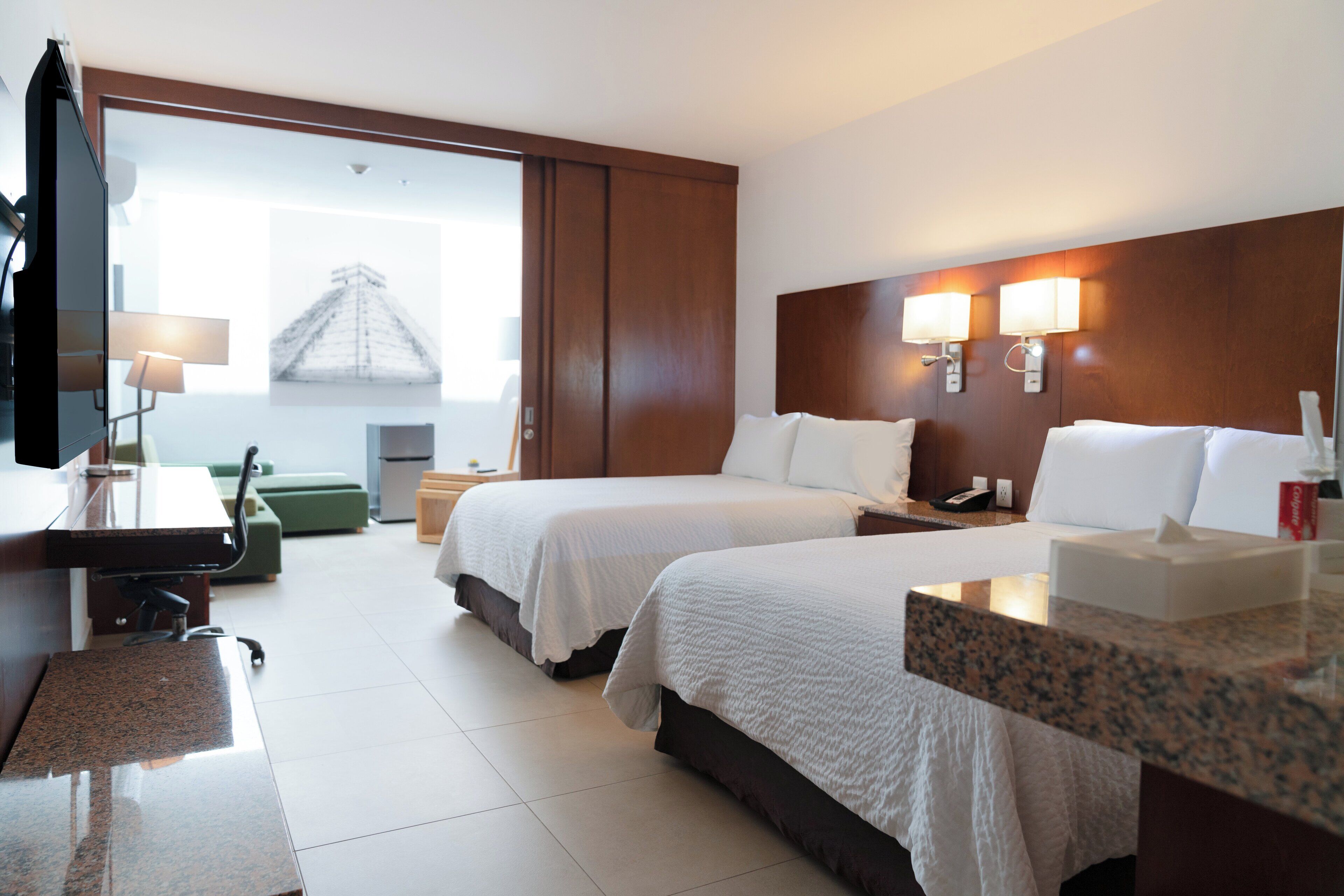 A hotel room with two beds, a desk, a television, and a window with a view of a pyramid.
