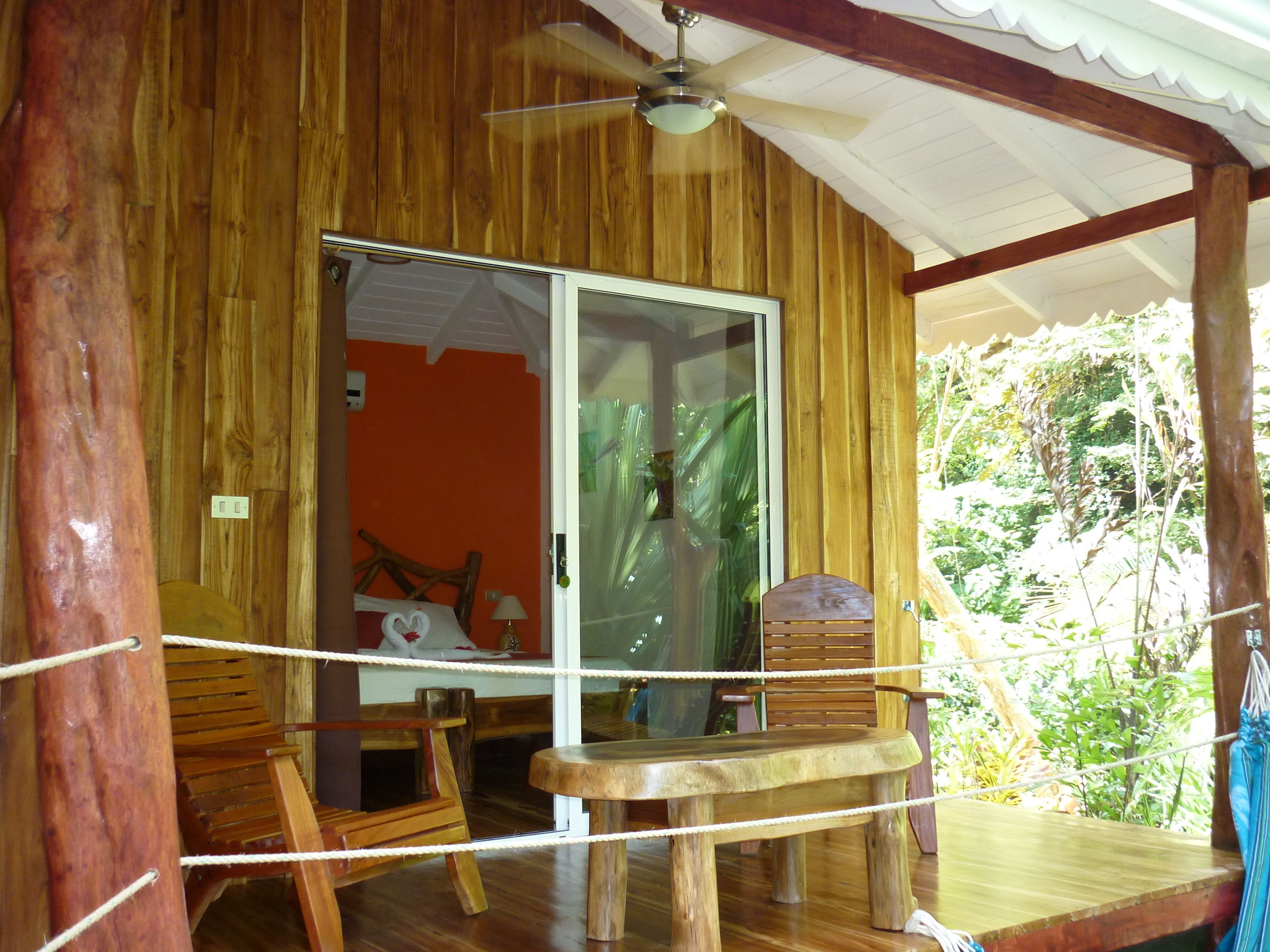 Eine Holzhütte mit Glastür, einem Deckenventilator und einer Holzterrasse mit Hängematte.