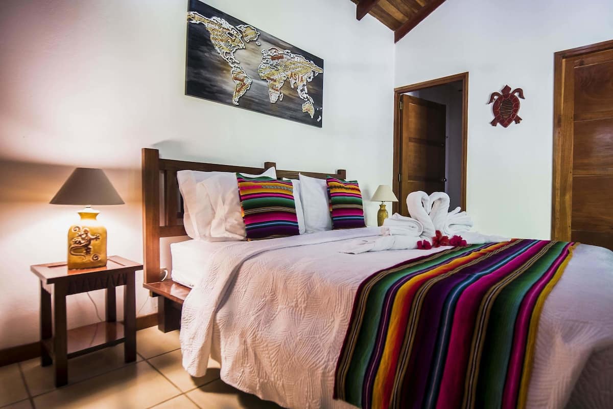 A neatly made bed with a colorful striped blanket, a world map on the wall, and a wooden door.