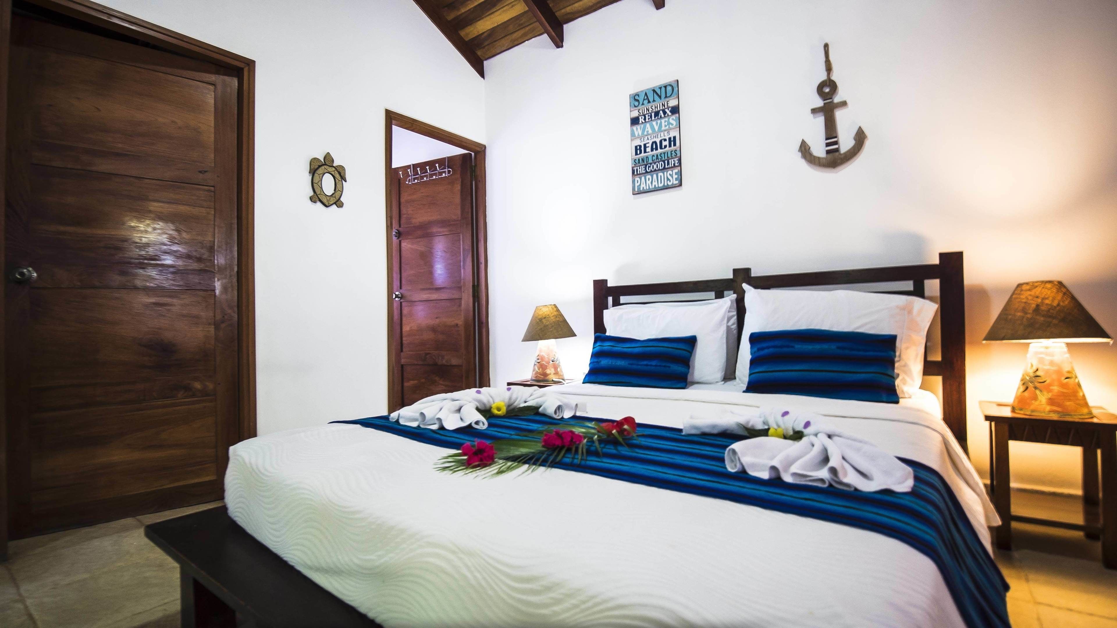 Una cama bien tendida con ropa de cama azul y blanca, una puerta de madera, y una pared con un letrero de temática náutica y una decoración de ancla.