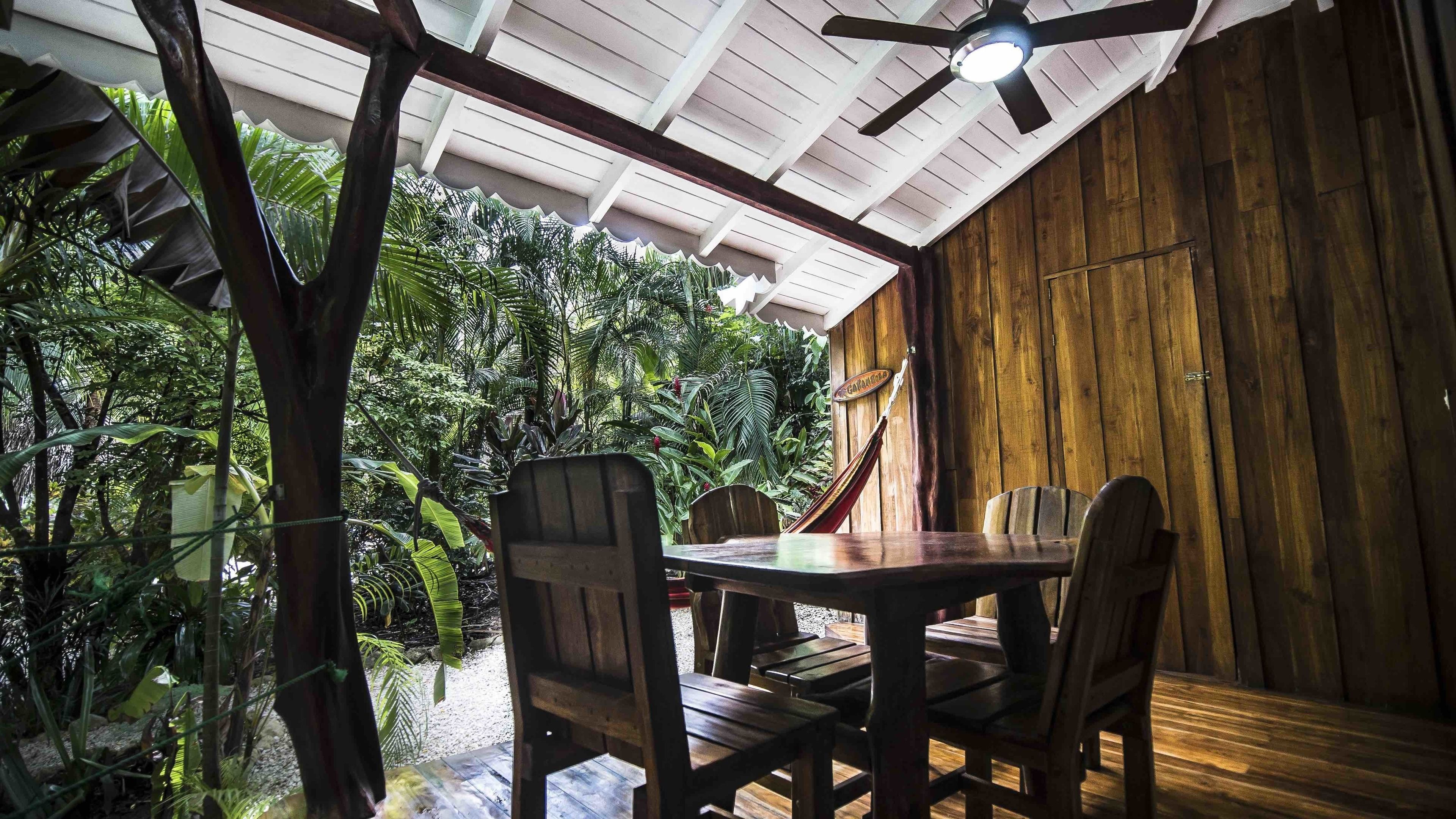 An indoor dining area with a wooden table and chairs, surrounded by lush tropical plants.