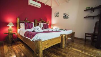 A wooden bed with a red wall, a small table with a lamp, and a chair.