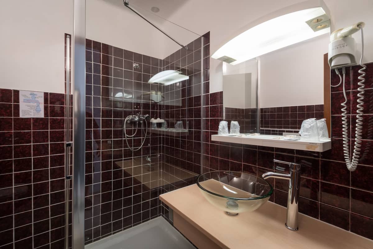 Ein Badezimmer mit einem Waschbecken aus Glas, einer Handbrause und einem an der Wand befestigten Föhn.