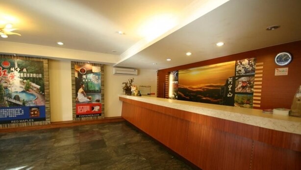 A hotel reception area with a wooden reception desk, a clock, and various posters on the walls. - Da San Tong Hotel (Chiayi City)