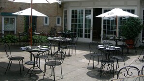 An outdoor patio area with tables and chairs, white umbrellas, and a brick building in the background. - The Lincklaen House (Cazenovia)