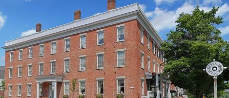 A historic red brick building with a white trim, multiple windows, and a sign indicating it is a hotel.