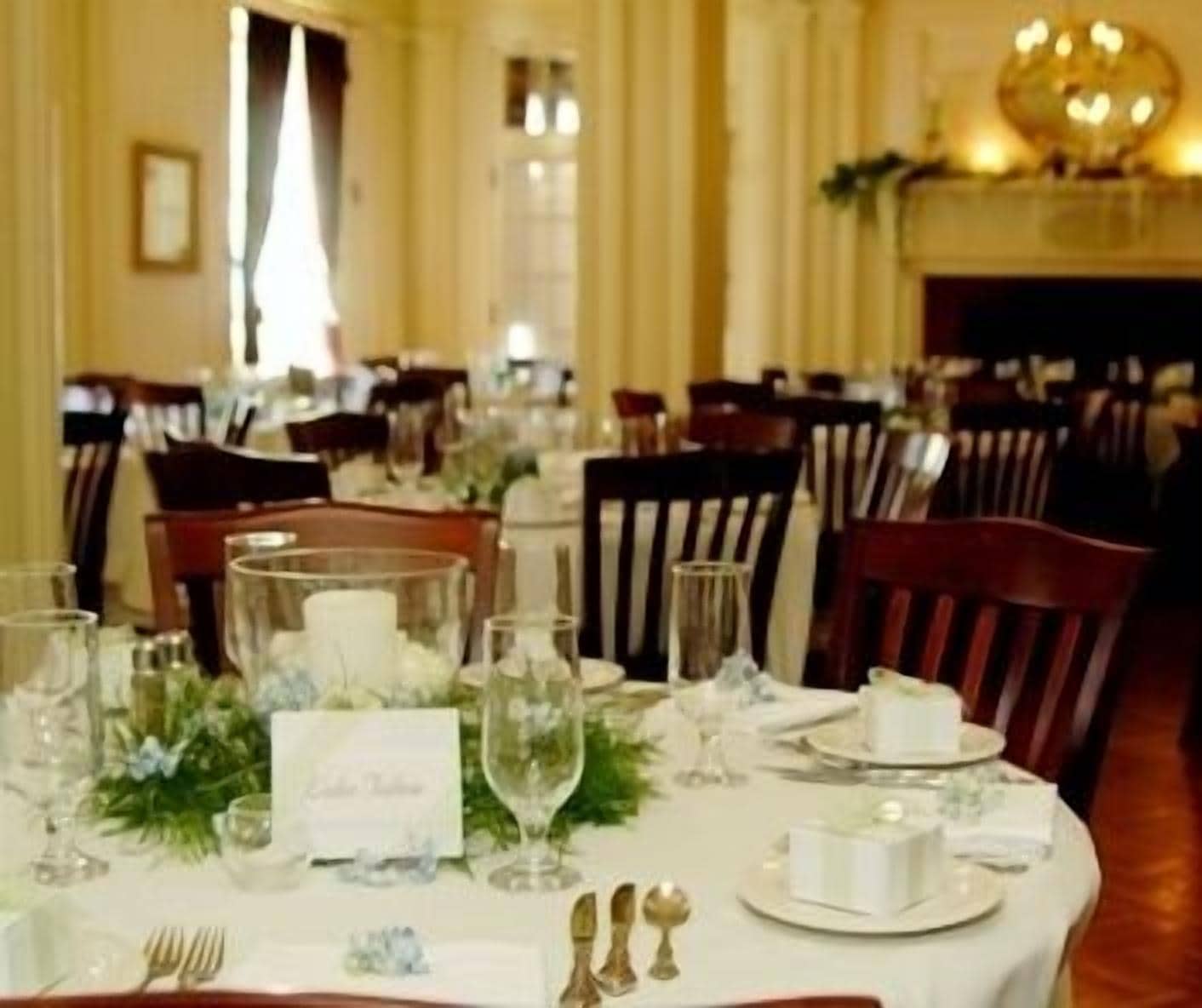 Une salle à manger élégante, avec des tables dressées pour le repas, agrémentée de nappes blanches, de verres et de compositions florales.
