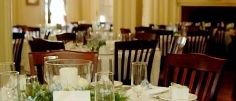 Une salle à manger élégante, avec des tables dressées pour le repas, agrémentée de nappes blanches, de verres et de compositions florales.