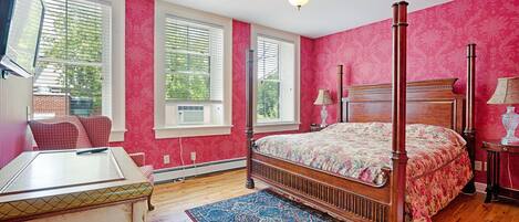 A bedroom with a four-poster bed, a wooden desk, and a red patterned wall.