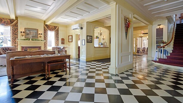 A hotel lobby with a checkered floor, a reception desk, a staircase, and a fireplace. - The Lincklaen House (Cazenovia)