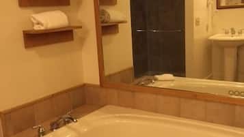 A bathroom with a large bathtub, a sink, and a mirror. There are towels on shelves and a shower visible in the background.