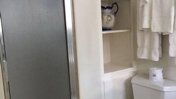 A bathroom with a toilet, a shelf with decorative items, and a shower enclosure.