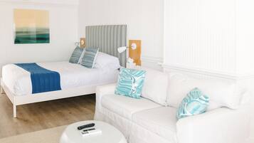 A bedroom with a bed, a white sofa, a round ottoman, and a ceiling fan.