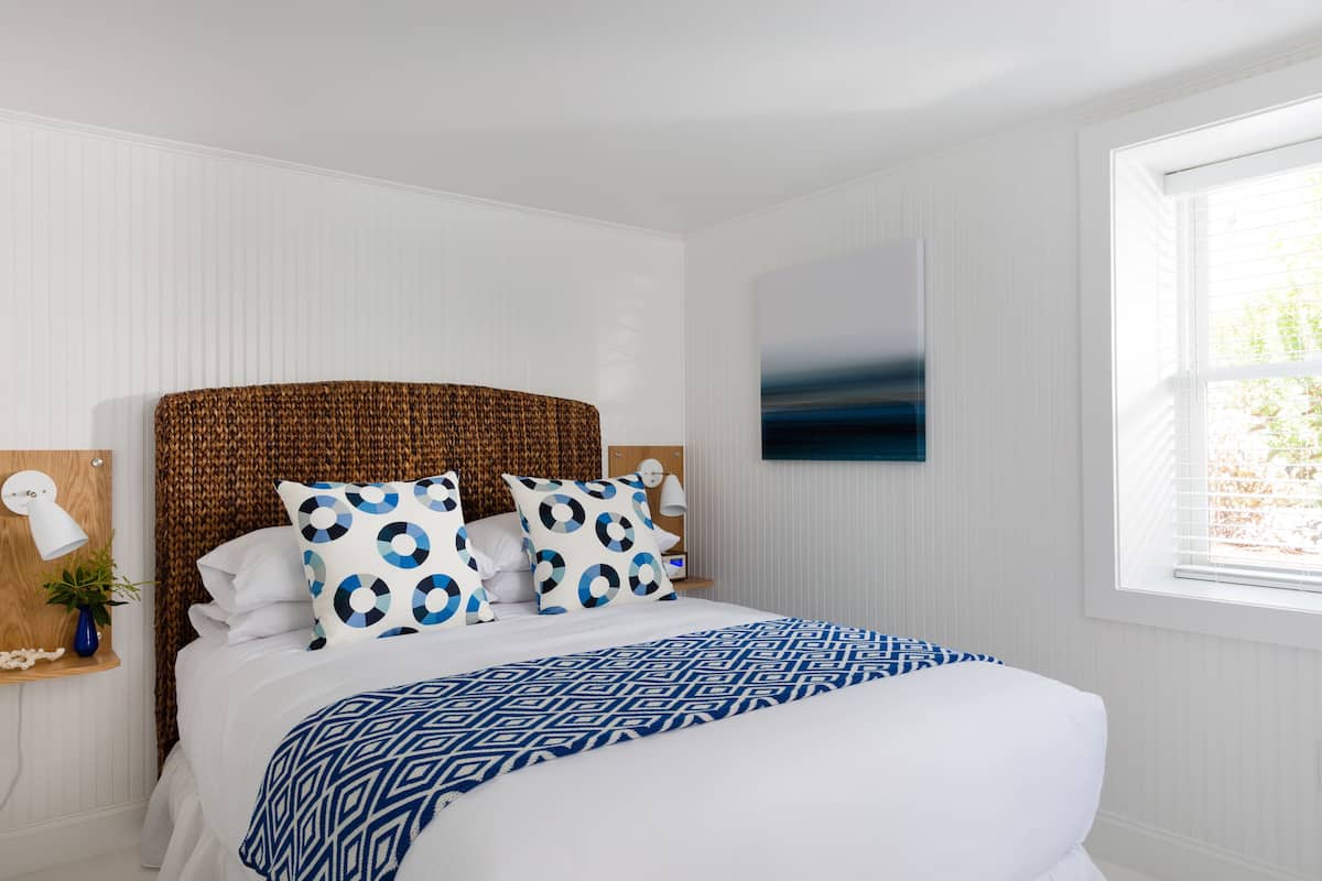 A neatly arranged bedroom with a large bed, a headboard, and a window with blinds.