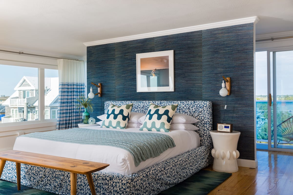 A bedroom with a large bed, a bedside table, a nightstand, and a window with a view.