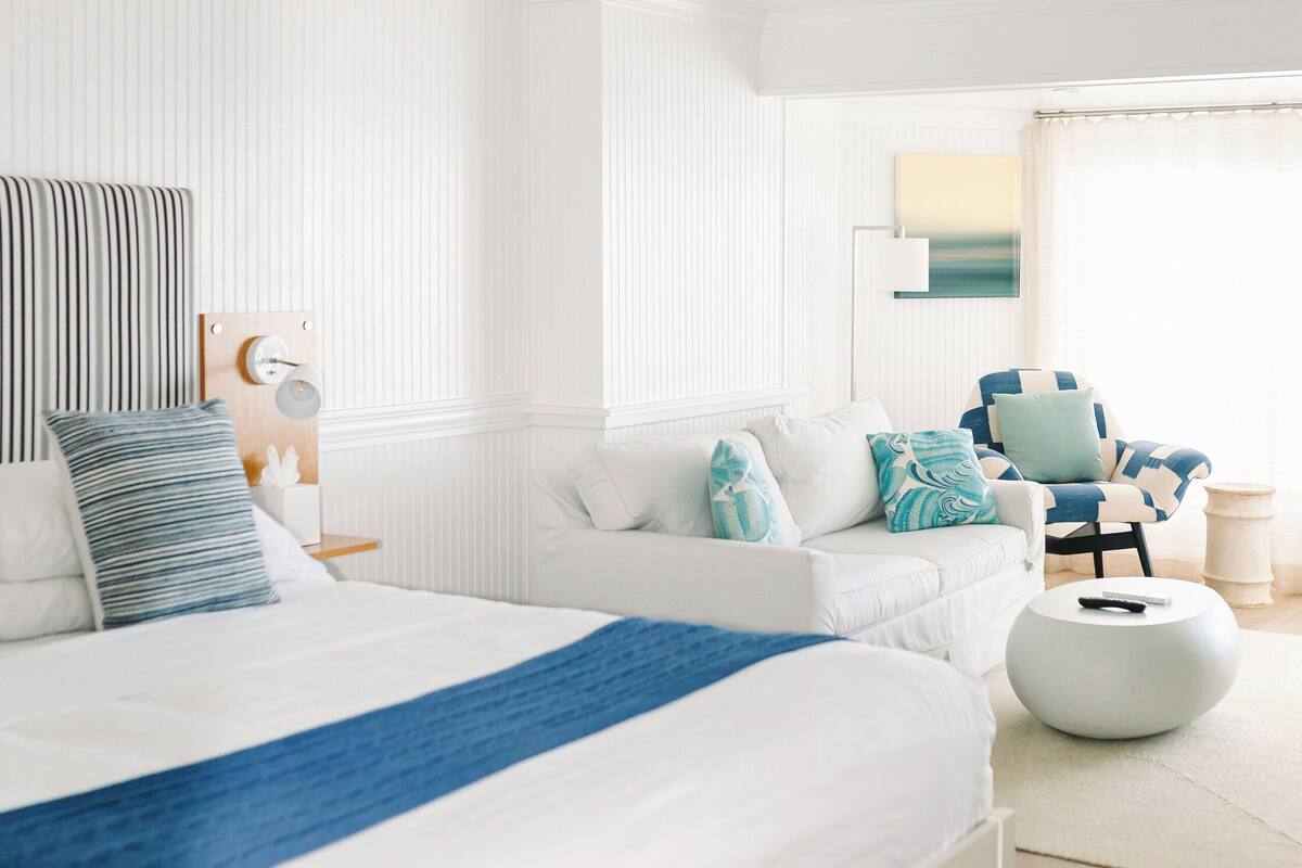 A modern bedroom with a large bed, a ceiling fan, a side table, and a chair.
