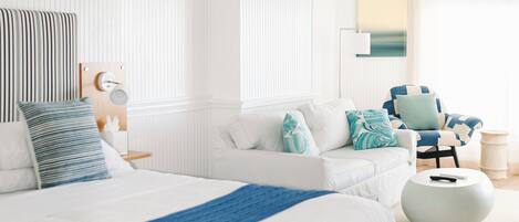 A modern bedroom with a large bed, a ceiling fan, a side table, and a chair.