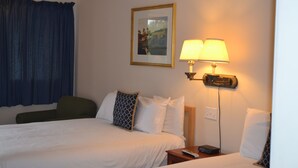 A hotel room with a bed, two bedside lamps, a nightstand, a remote control, and a framed picture on the wall. - Henniker Motel (Henniker)