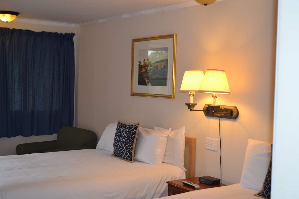 Habitación de hotel con cama, dos lámparas de noche, mesita de noche, control remoto y un cuadro en la pared.