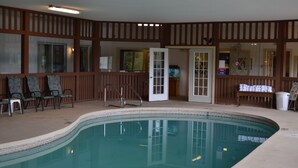 An indoor swimming pool with a tiled edge, wooden paneling, and a door leading to another room. - Henniker Motel (Henniker)