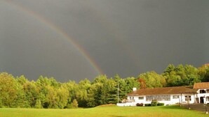 A house with a large lawn and a rainbow in the sky. - Henniker Motel (Henniker)