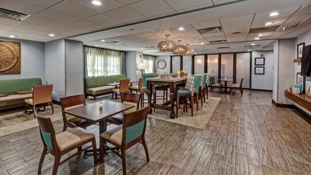 A hotel lobby with a dining area, sofas, and a large decorative wall piece. - Hampton Inn Summerville SC (Summerville)