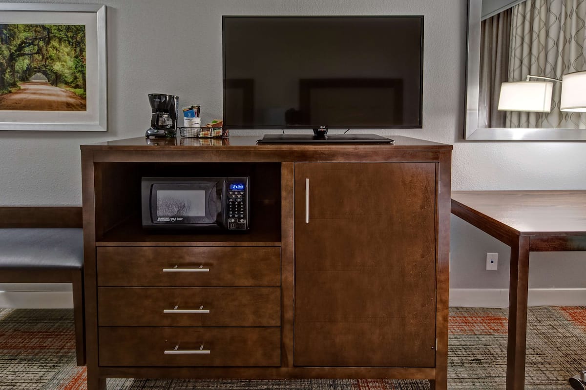 A wooden cabinet with a microwave, a coffee maker, and a flat-screen TV on top.