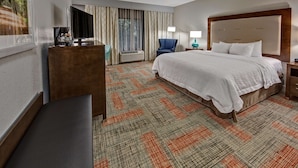 A hotel room with a large bed, a desk with a coffee maker, a chair, a TV, and a window with curtains. - Hampton Inn Summerville SC (Summerville)