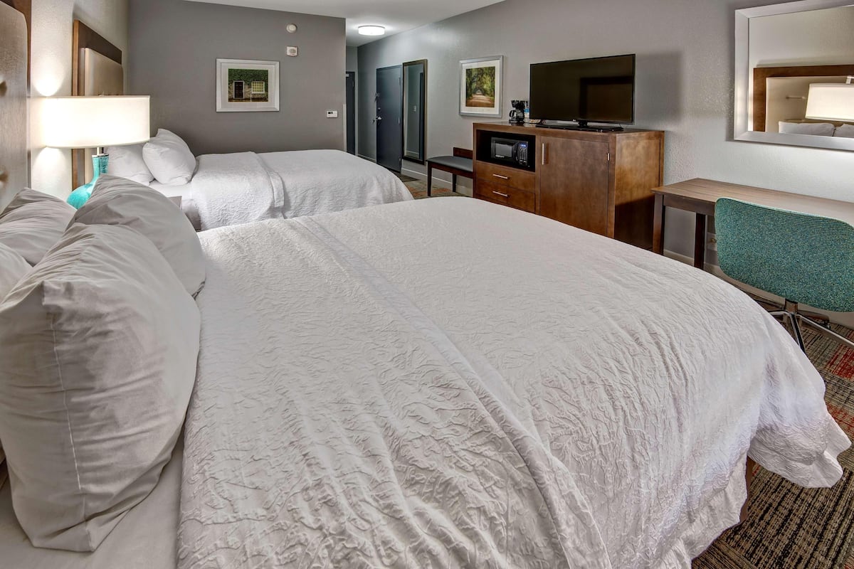A hotel room with two beds, a desk, a television, and a mirror.